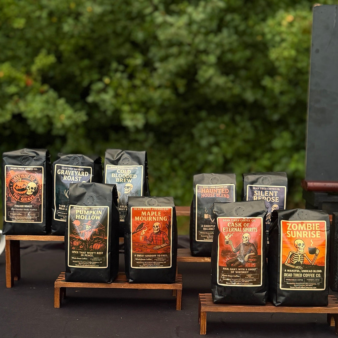A lineup of real Dead Tired Coffee Co. bags at a booth, including Haunted House, Silent Repose, and Cask of Eternal Spirits