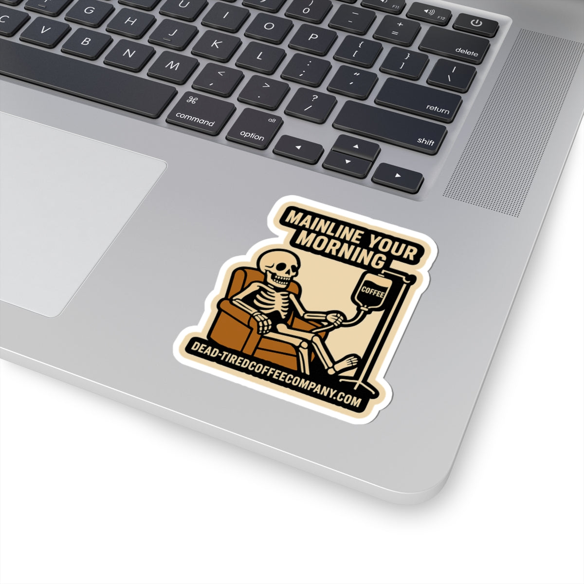 Laptop with a skeleton sticker reading 'Mainline Your Morning' on a white background